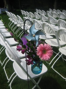 Jars containing orchids, gerbera daiseys, and roses along with colorful pinwheels decorated chair rows.